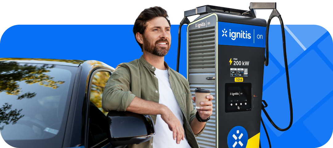 Šypsantis vyras su kavos puodeliu stovi prie elektromobilio ir „Ignitis ON“ įkrovimo stotelės.