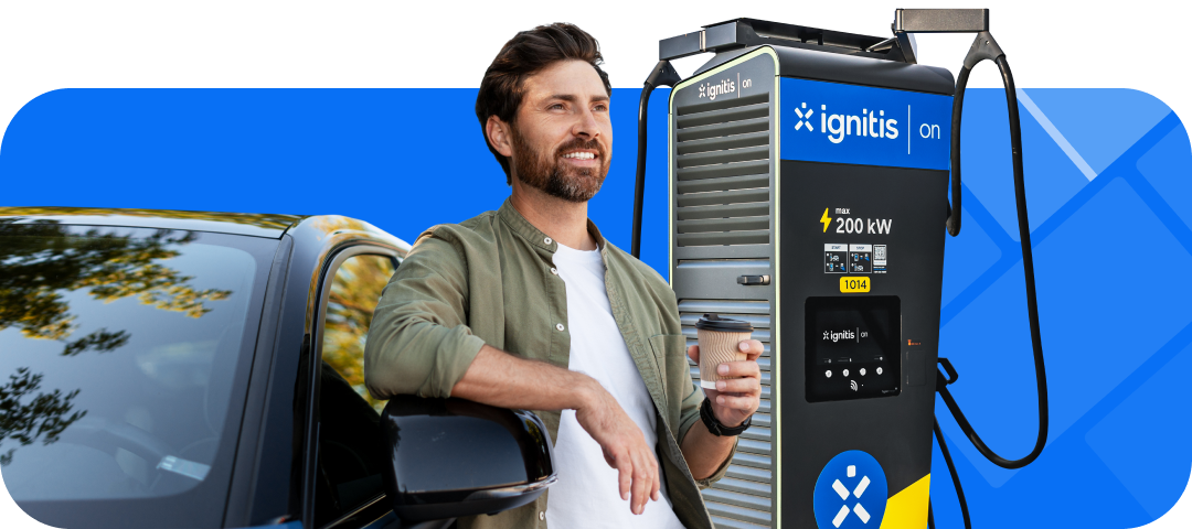 Vyras su kavos puodeliu prie „Ignitis ON“ įkrovimo stotelės ir elektromobilio.