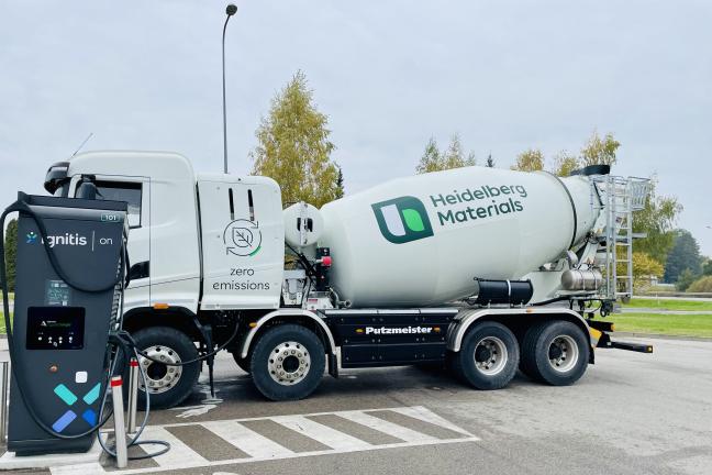 Baltas „Heidelberg Materials“ betono maišytuvas su „zero emissions“ (nulinių emisijų) ženklu stovi įkraunamas iš „Ignitis ON“ stotelės lauko aikštelėje