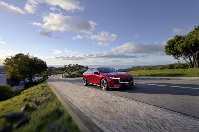 Raudona Mazda 6e važiuoja asfaltuotu keliu saulėtą dieną