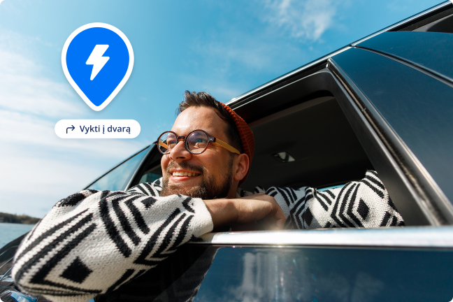 Vyras iškišęs galvą per elektromobilio langą šypsosi ir džiaugiasi kelionėmis po Lietuvos dvarus.