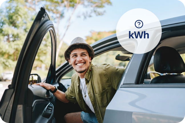 Vyras lipdamas iš elektromobilio šypsosi, nes džiaugiasi sužinojęs kiek kWh reikia nuvažiuoti 100 km elektromobiliu.