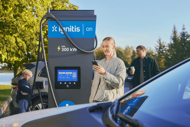 Ignitis ON itin greito elektromobilių įkrovimo stotelė ir laiminga šeima, kuri joje įsikrauna savo elektromobilį.