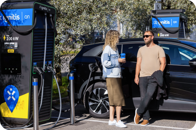 Moteris geria kavą ir kalbasi su vyru, kol jų elektromobilis kraunasi Ignitis ON greitoj įkrovimo stotelėje.