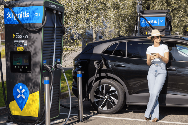 Moteris atsirėmusi į elektromobilį ilsisi, kol jis kraunasi Ignitis ON itin greito įkrovimo stotelėje.